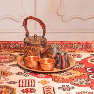 An ornate, engraved copper tea set displayed on a vibrant, traditional patterned rug.